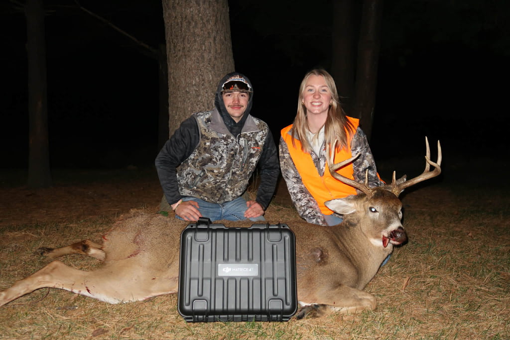 Two people posing at night with a recovered whitetail buck and drone case after a successful drone deer recovery in Wisconsin by Wisco Drone Co.