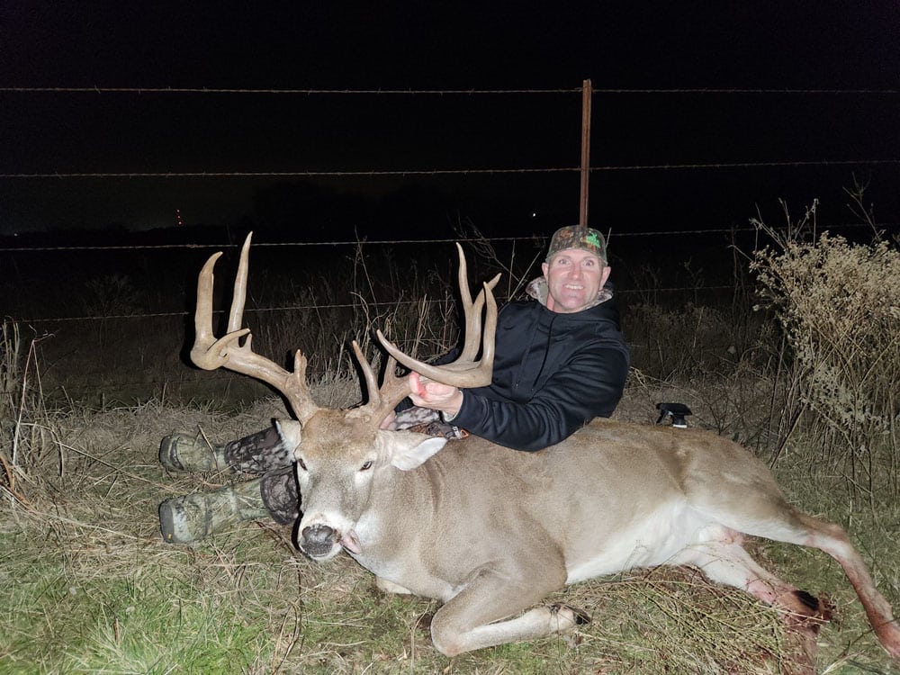 Hunter posing at night with a large trophy whitetail buck after a successful deer recovery in Wisconsin with Wisco Drone Co.